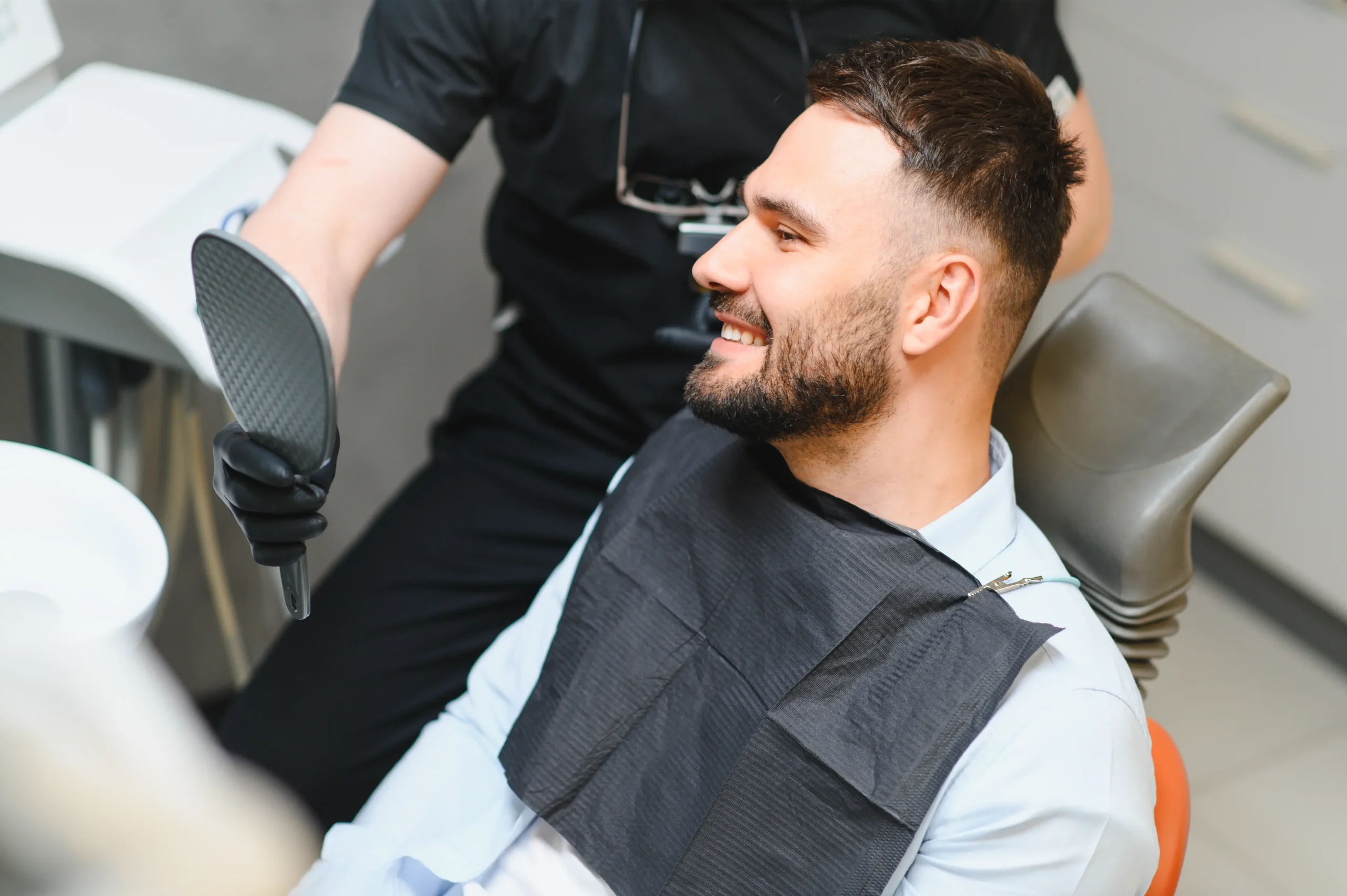 Smiling man checking his teeth in a hand mirror