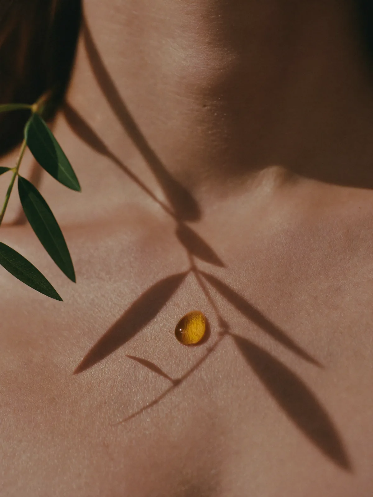 Close-up of skin with a drop of facial oil and leaf shadows